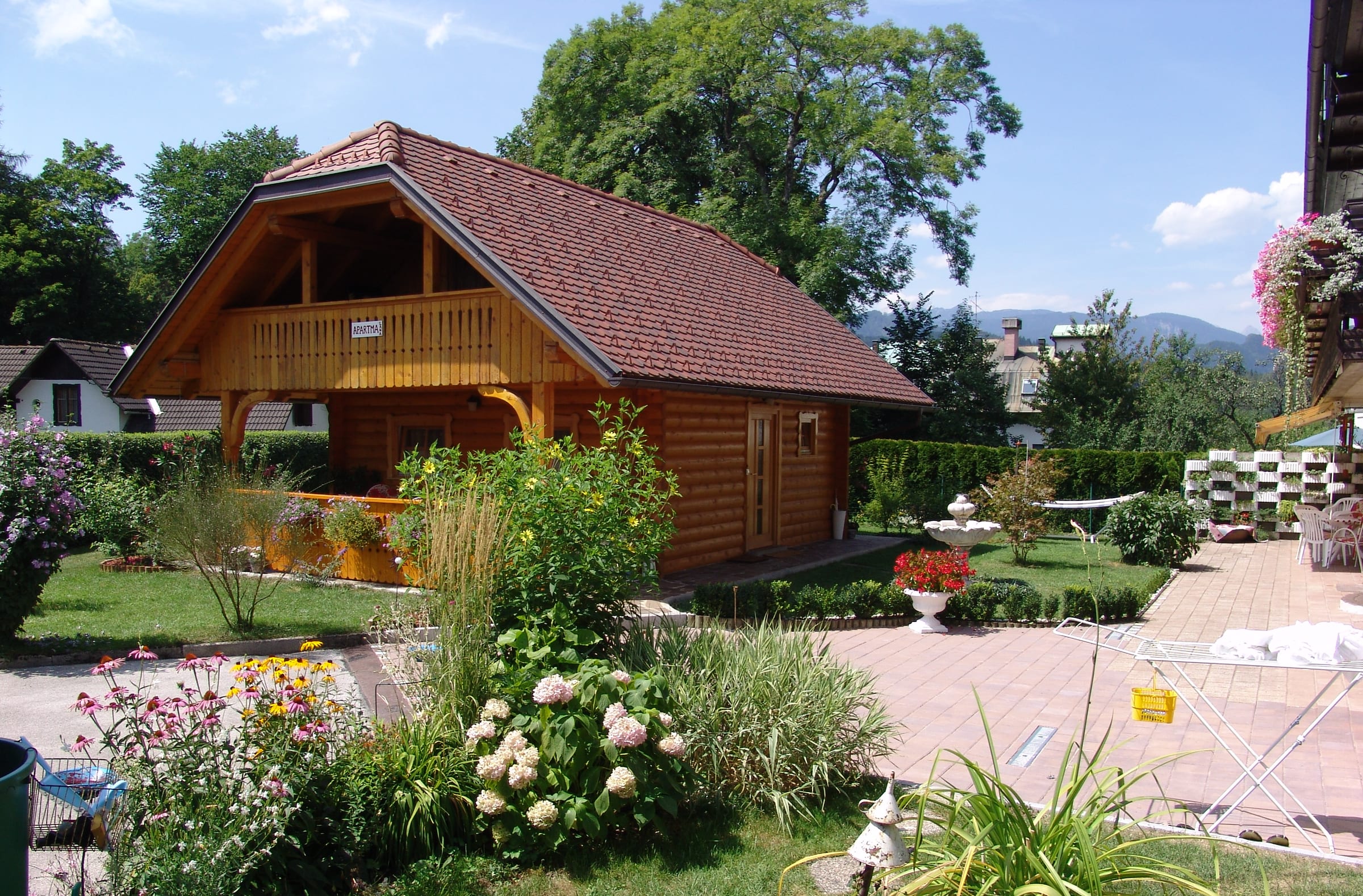 The planted garden in summer, with roses and shrubs in front of the timber chalet and hills beyond.