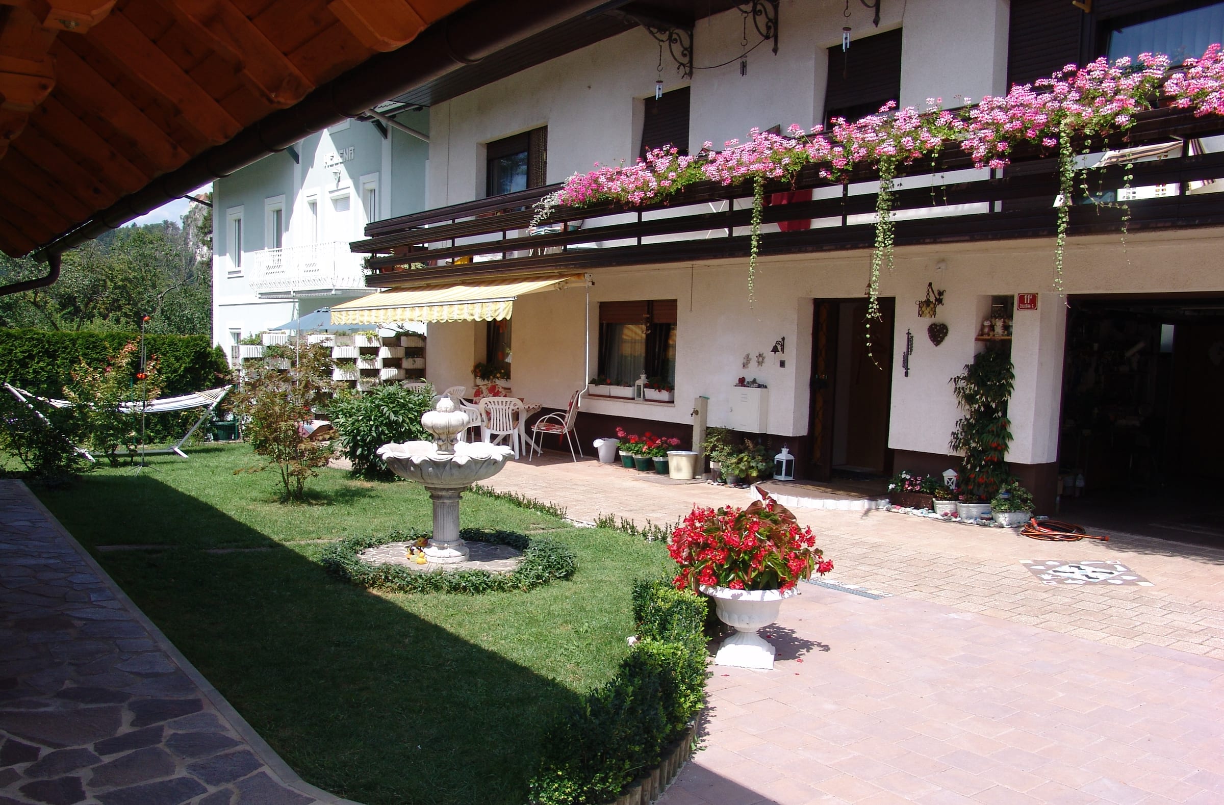The house seen along its length, with flower-filled balconies above a lawn and a paved garden path.